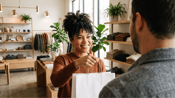 Titolare di una piccola impresa che consegna una busta per gli acquisti di una boutique a un cliente al checkout.