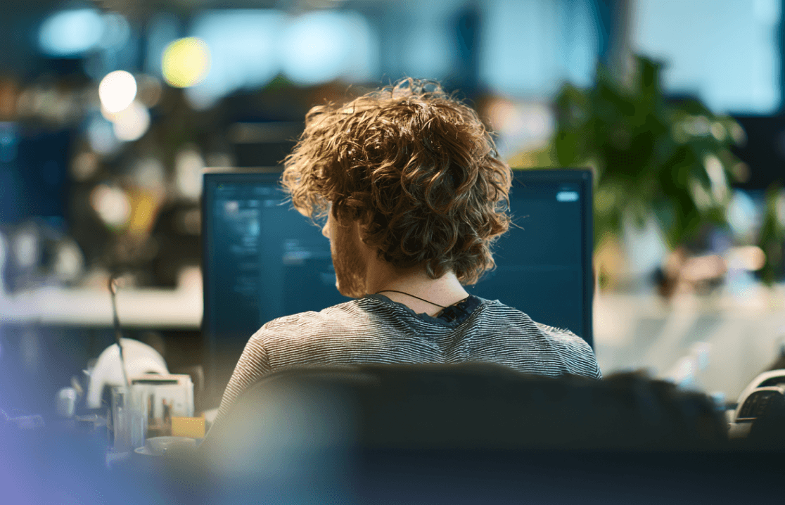 Inquadratura alle spalle di uno sviluppatore con i capelli ricci che lavora al computer in un ufficio moderno.